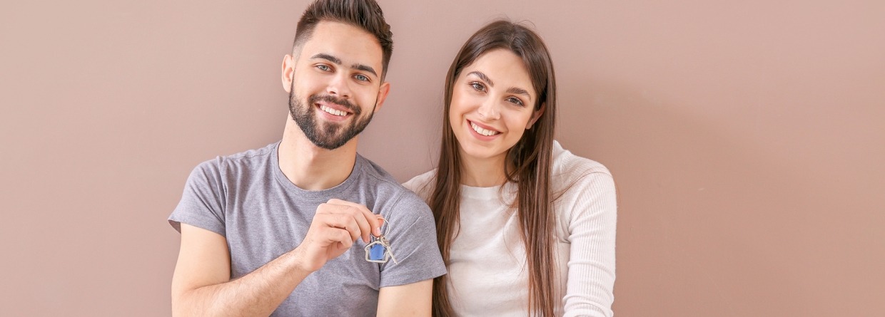 Jon stel met huissleutels van hun nieuwe huis in hun hand zitten voor een gekleurde muur